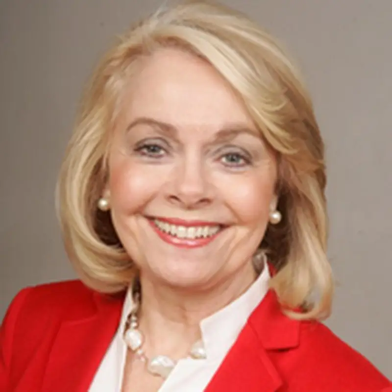 Betty Sue Flowers, Coacharya board member, smiling in a red blazer and pearl necklace